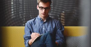 Blog 18 Person in Blue Denim Jacket Sitting on Chair While Writing