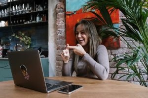 Blog 4 Smiling woman using sign language during a video call on a laptop in a stylish indoor setting.